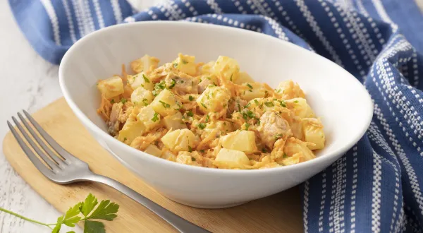 Fotografia em tons de azul em uma bancada de madeira com um pano listrado azul ao lado. No centro, um prato fundo branco com a salada de batata, atum, cebola e salsinha. Fotografia em tons de azul em uma bancada de madeira com um pano listrado azul ao lado. No centro, um prato fundo branco com a salada de batata, atum, cebola e salsinha.